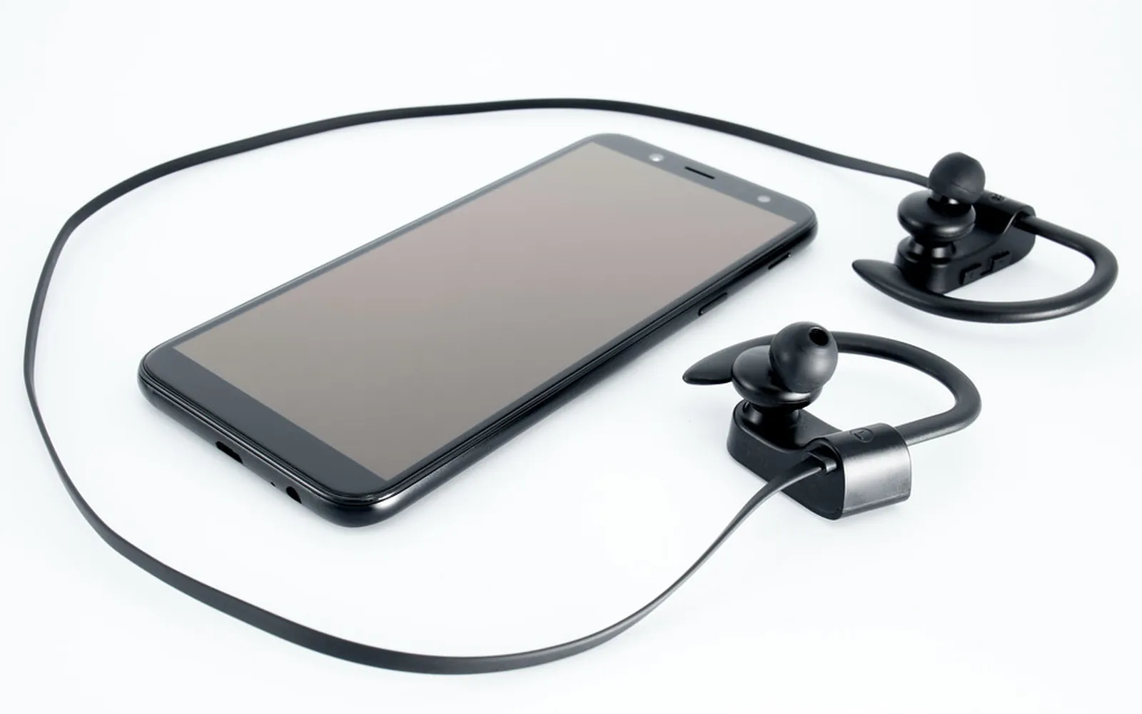 Wireless Bluetooth earphones lying next to a smartphone on a white surface